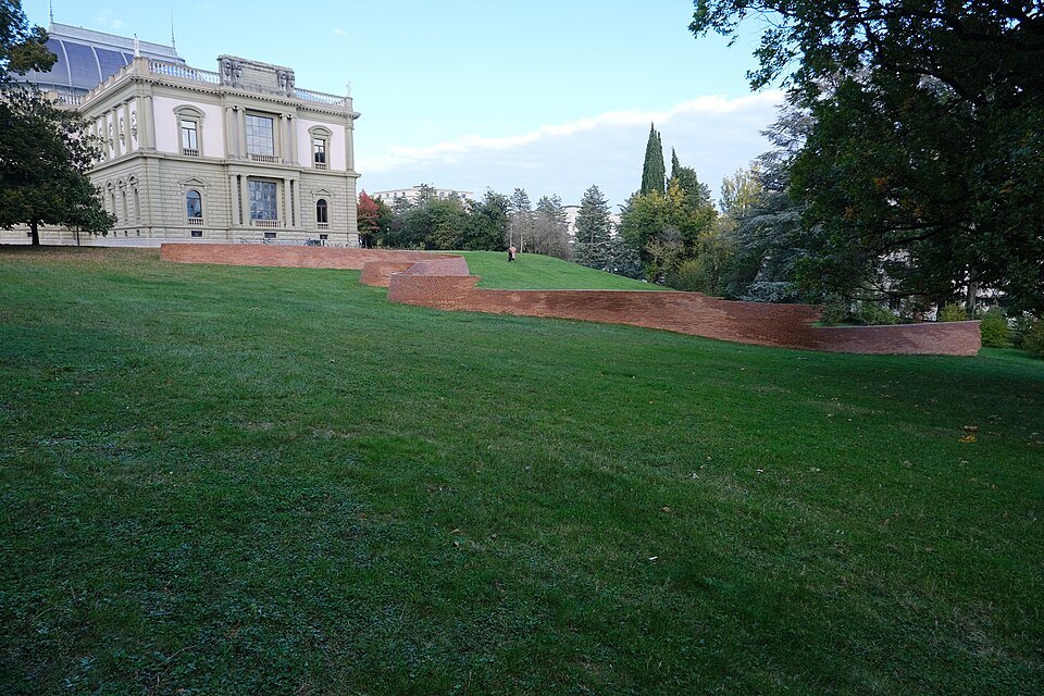 A low brick wall winding across the lawn below the Musée Ariana