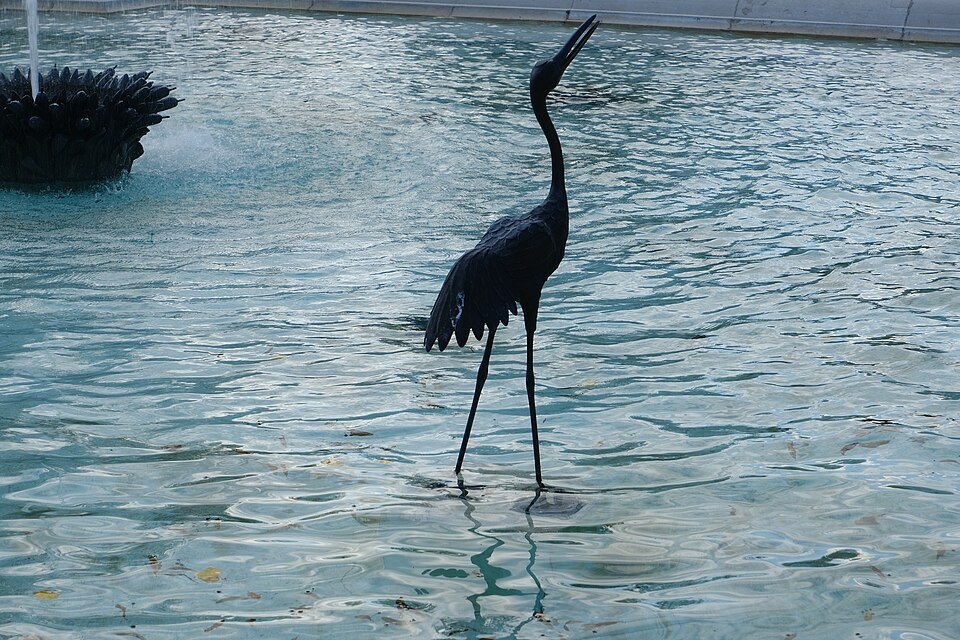 A bronze heron standing in the fountain of the Ariana park