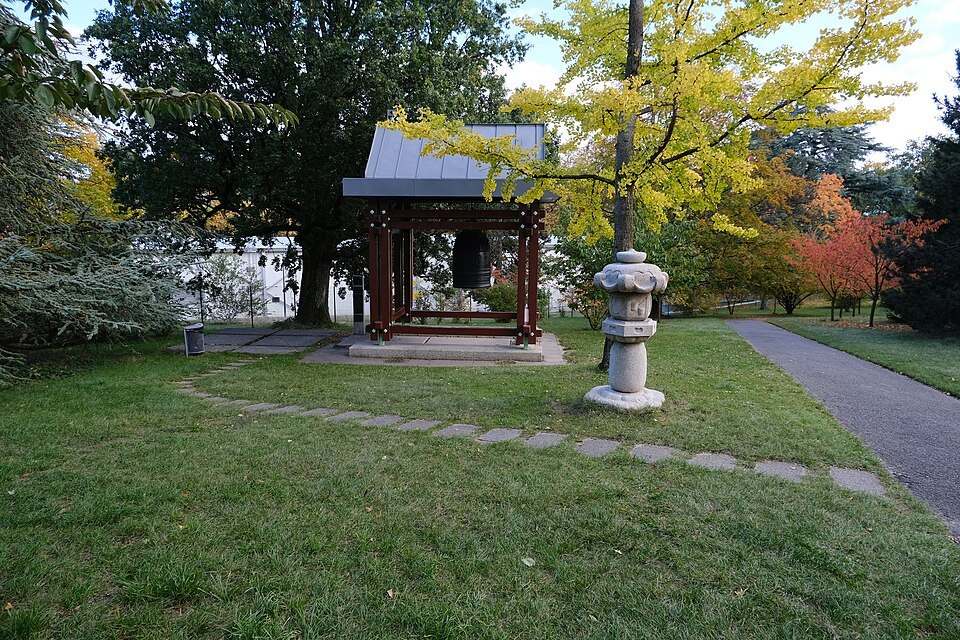 The Shinagawa bell under its wooden shelter beside a stone lantern in the Ariana park