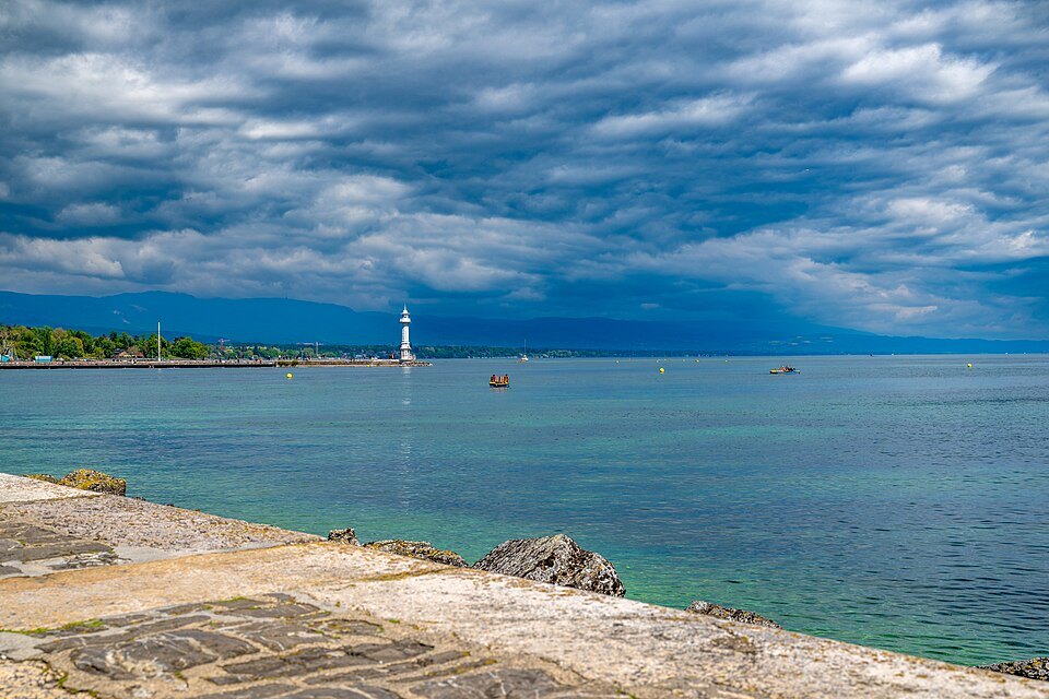 The Pâquis lighthouse under a heavy sky, seen from the rocks of the shore