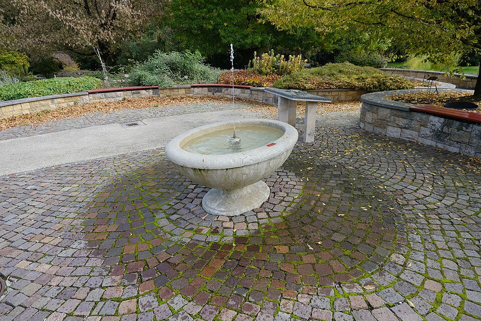 A stone fountain on a cobbled circle in the Terres de Pregny part of the garden
