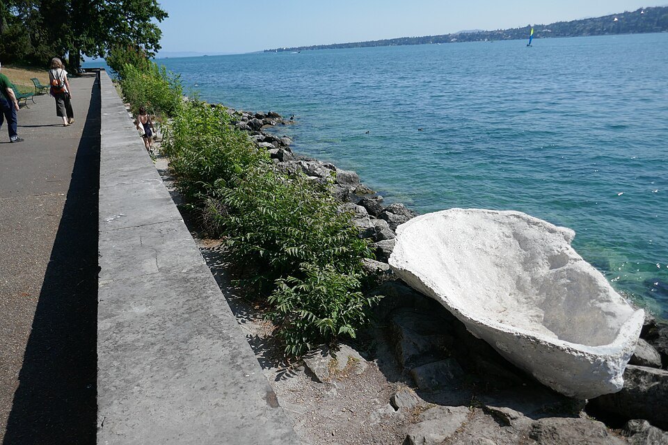 A white shell-shaped sculpture on the rocks beside the lakeside path