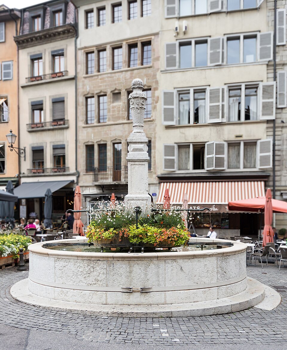 The flower-filled fountain of the Place du Bourg-de-Four in front of café awnings