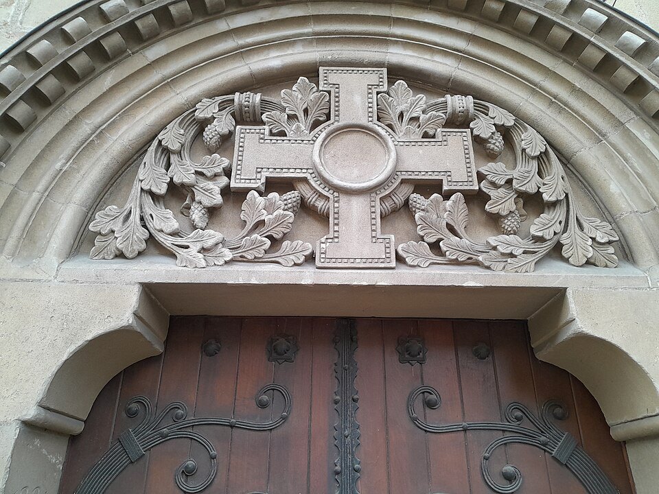 A carved cross and foliage over the wooden door of a cathedral portal