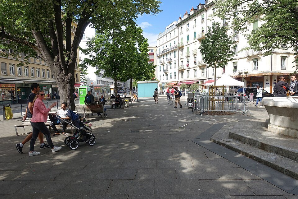 People walking under the trees of the Place de la Navigation in the Pâquis