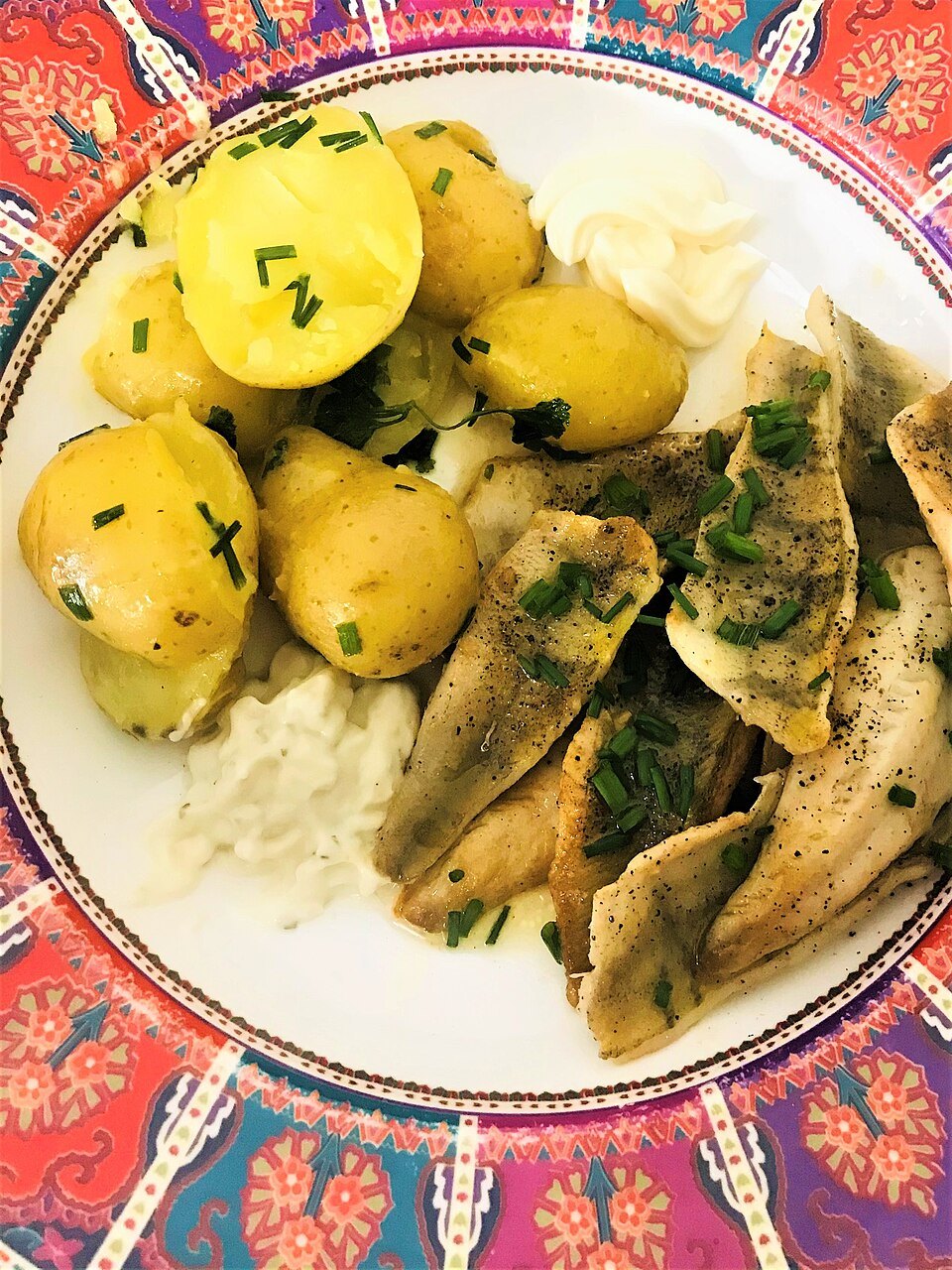 Perch fillets with herbs and boiled potatoes on a patterned plate