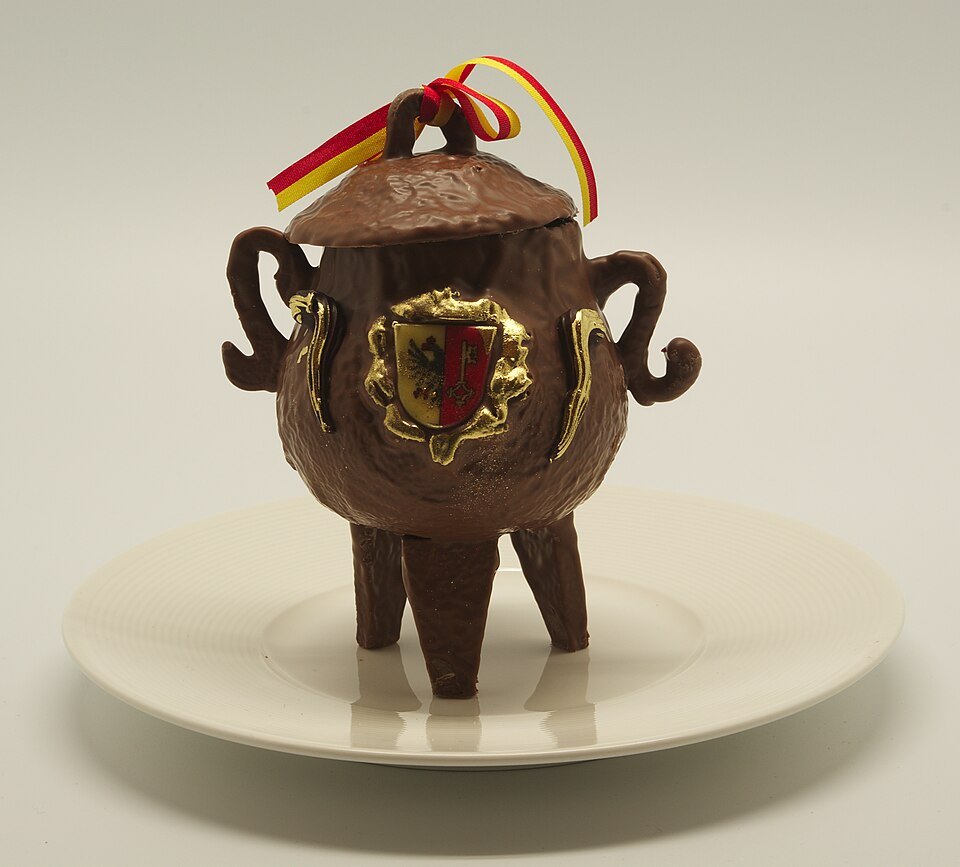 A chocolate marmite on a white plate, the Geneva shield on its side
