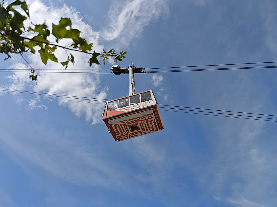 A red cabin of the Salève cable car overhead against a blue sky