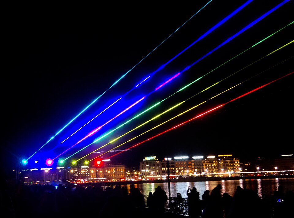 Colored laser beams fanning over the harbor at night during Geneva Lux