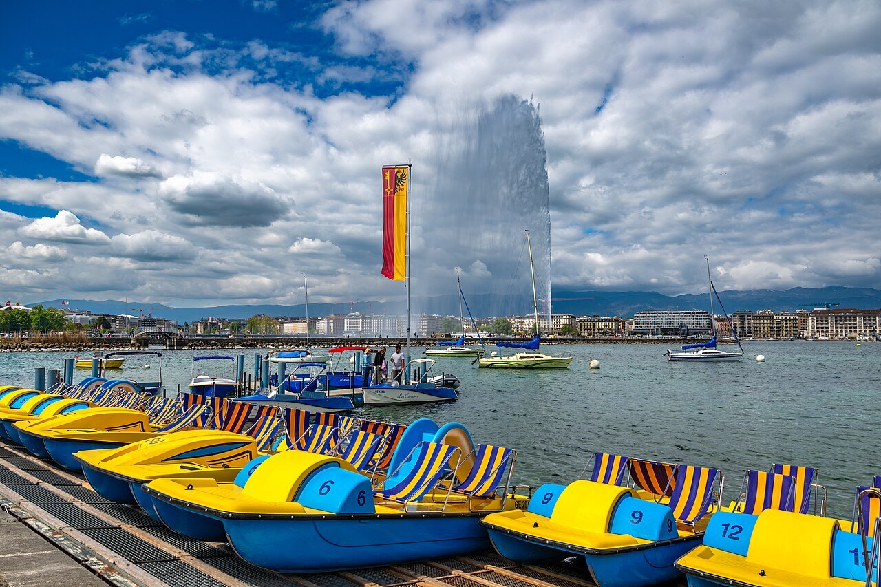 Pedal boats in Geneva colors at the harbor, the city flag and the Jet d'Eau rising over the Rade