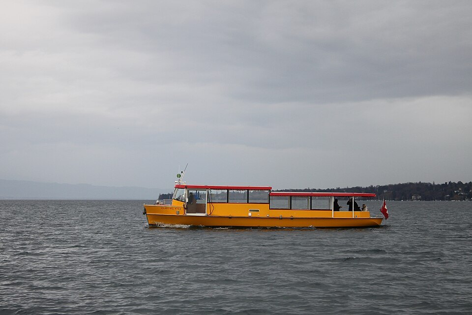 A yellow and red Mouette crossing the harbor on a gray day