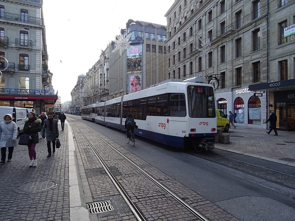 A tram running along a busy shopping street past pedestrians
