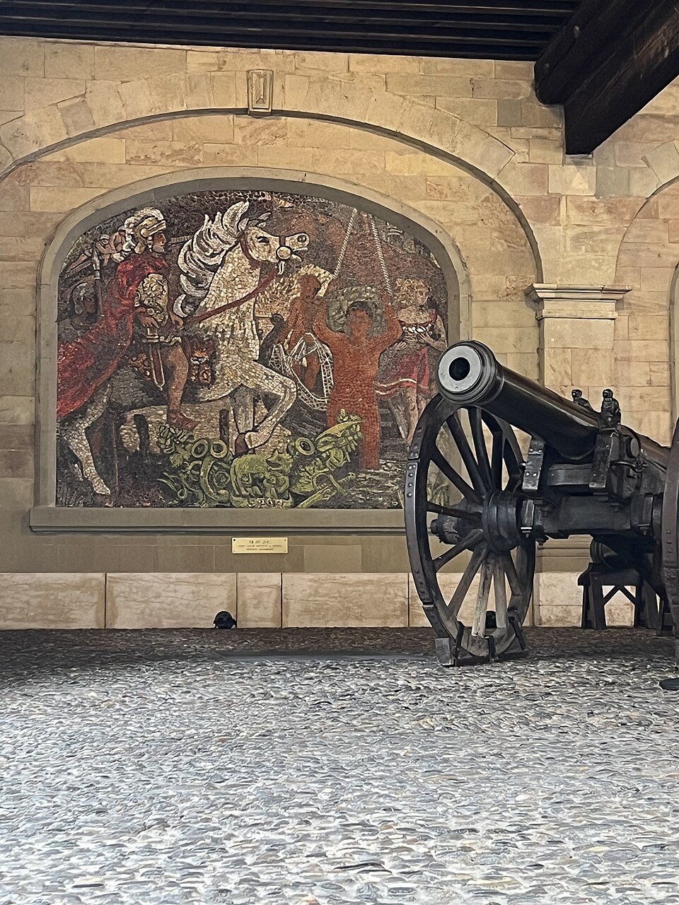 An old cannon under a painted mural in the arcade of the Old Arsenal