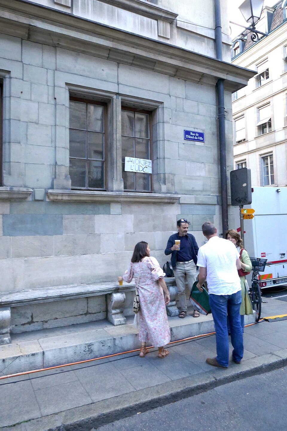 People passing a stone house on the Rue de l'Hôtel-de-Ville