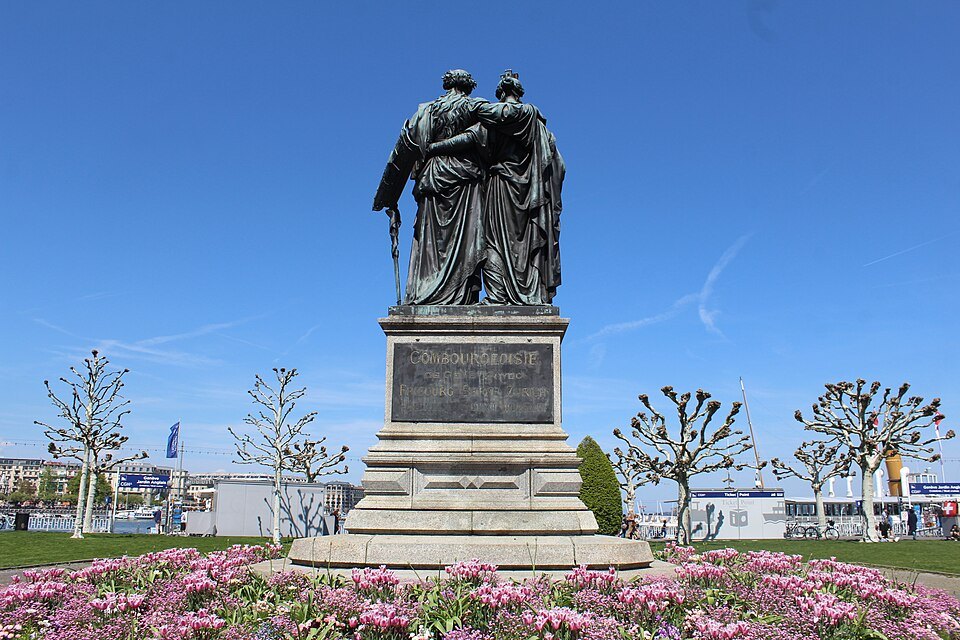 The National Monument in the Jardin Anglais, its two bronze women over a bed of pink flowers