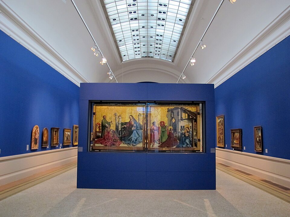 An altarpiece on a blue wall in a skylit painting gallery