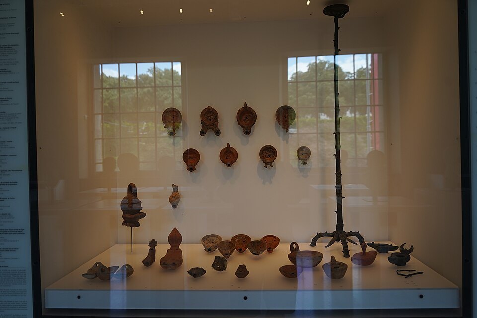 A display case of Roman oil lamps and a bronze lampstand in the museum