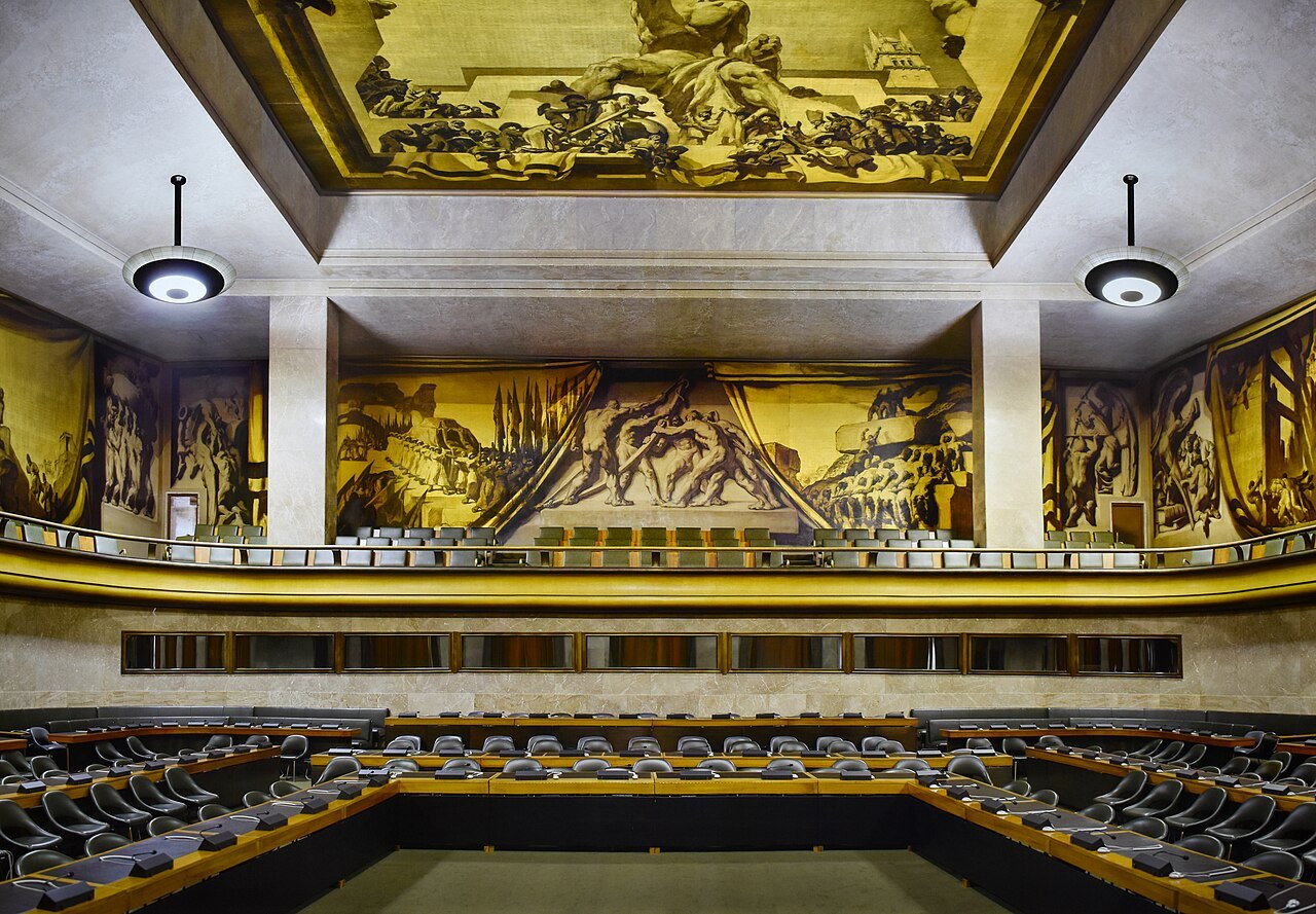 The gilded murals and circular seating of a council chamber in the Palace of Nations
