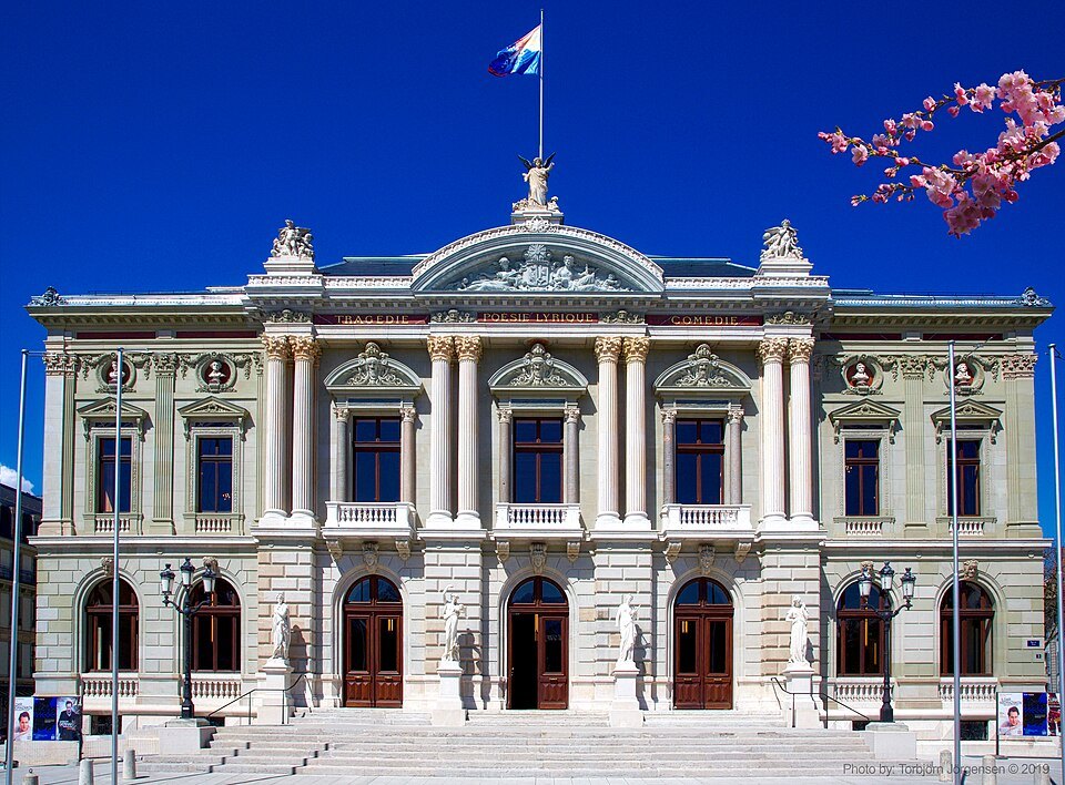 The Grand Théâtre's facade under a blue sky, a flowering branch in the corner