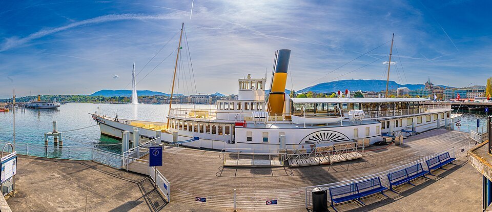 A paddle steamer at its landing stage on a bright day, the harbor behind