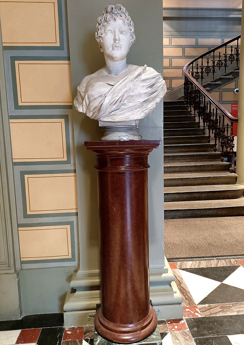 A marble bust of Germaine de Staël on a pedestal at the foot of a staircase